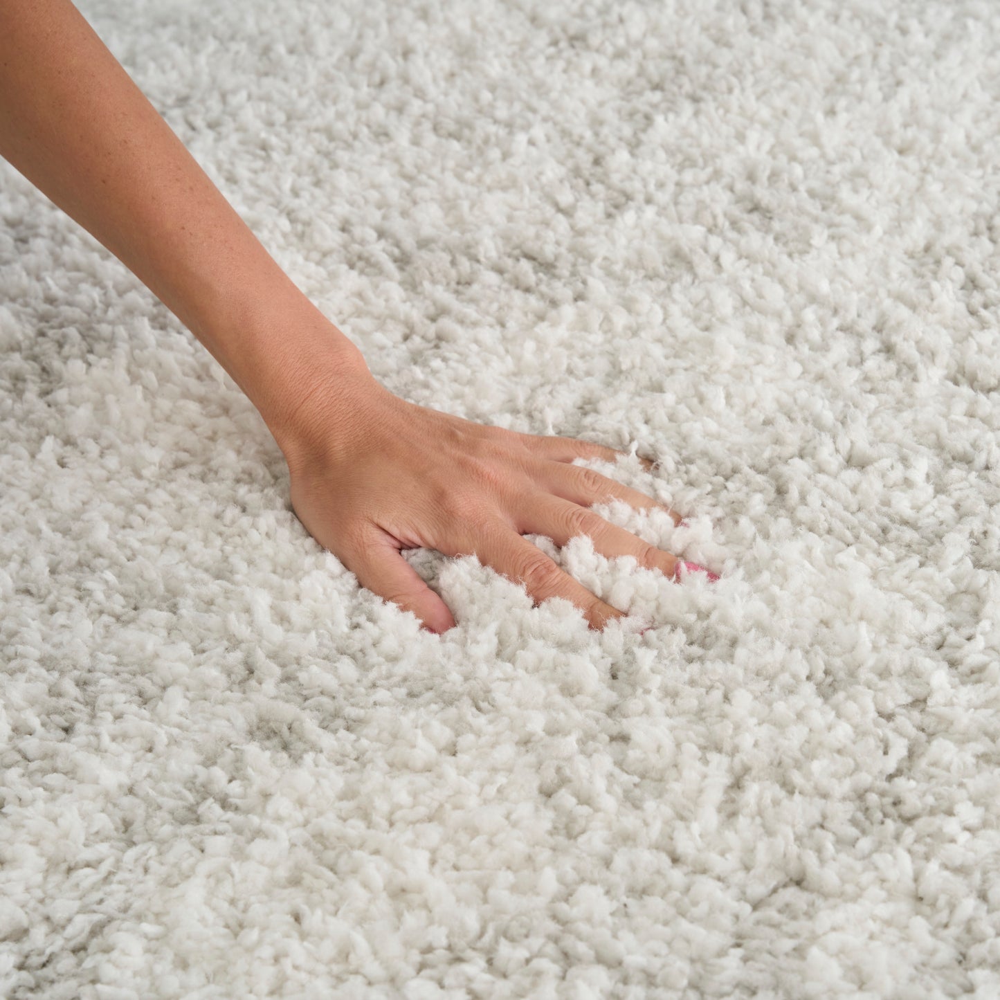 Hand presses into fluffy white shag carpet, highlighting soft, thick pile.