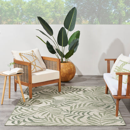 Cozy indoor patio with wood rattan chairs, white cushions, a leaf-patterned rug, and a large potted tropical plant.