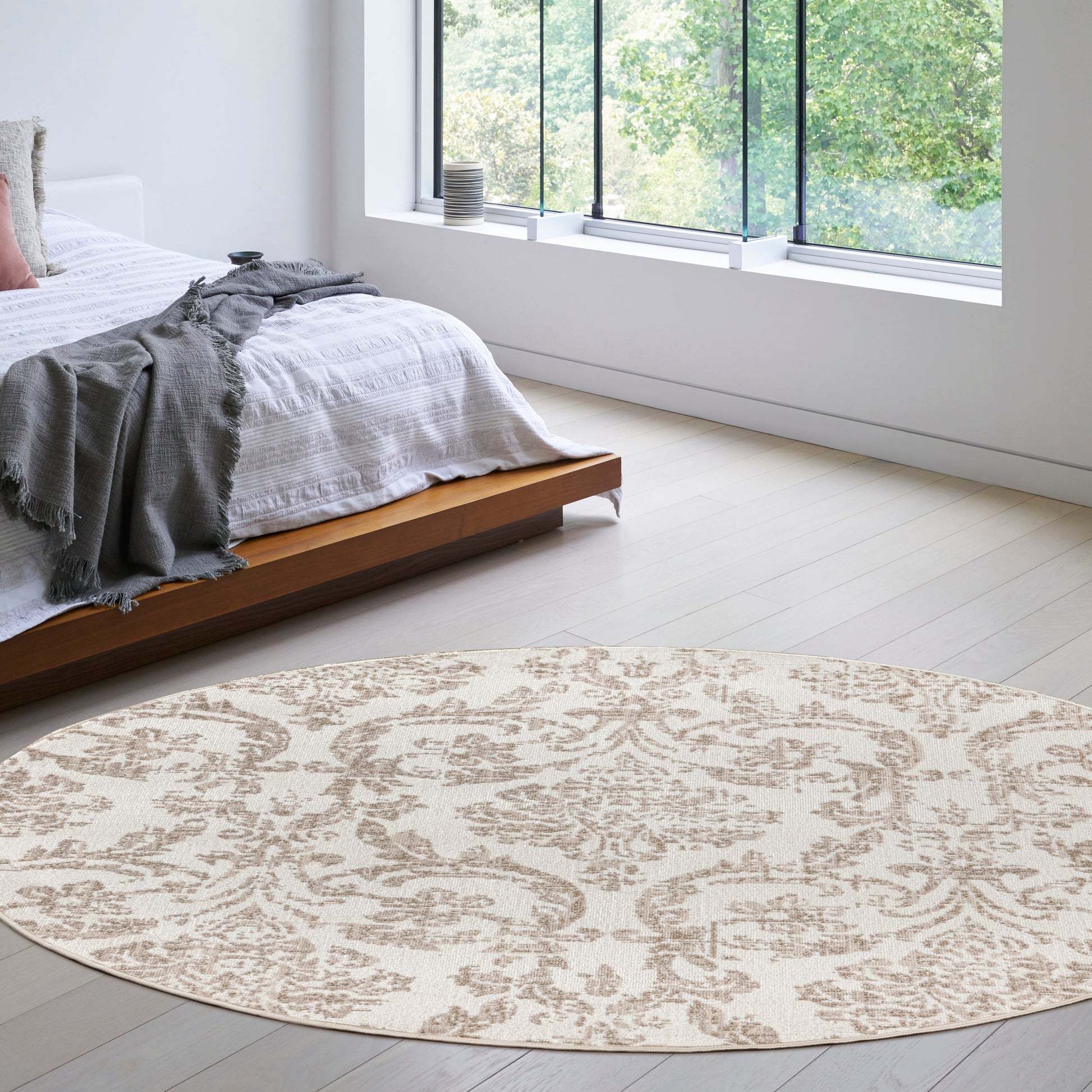 Round beige patterned area rug in a bright modern bedroom with white bedding and a low wood platform bed.