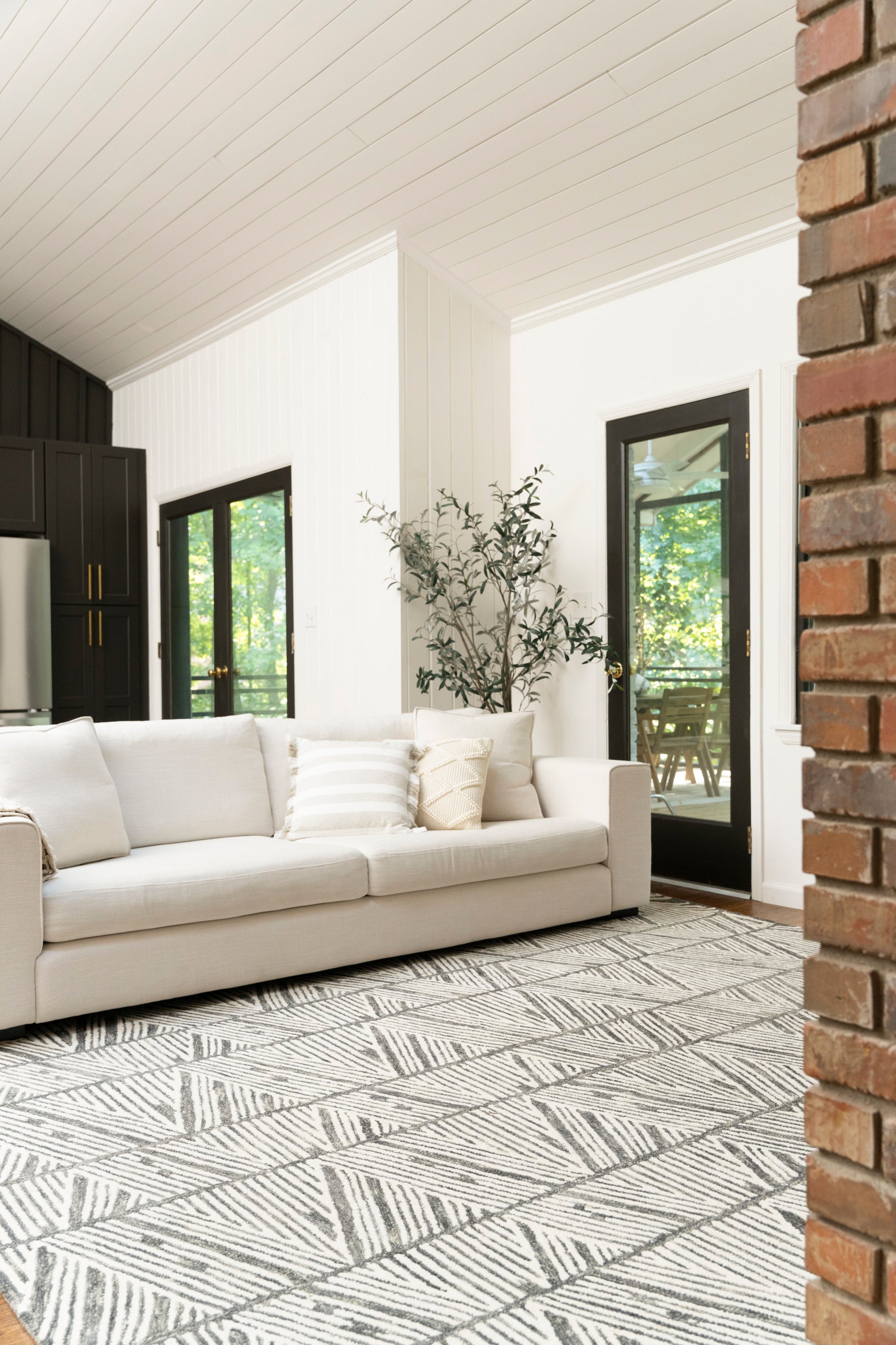 Light beige geometric leaf rug in a white-paneled living room with black-framed doors.