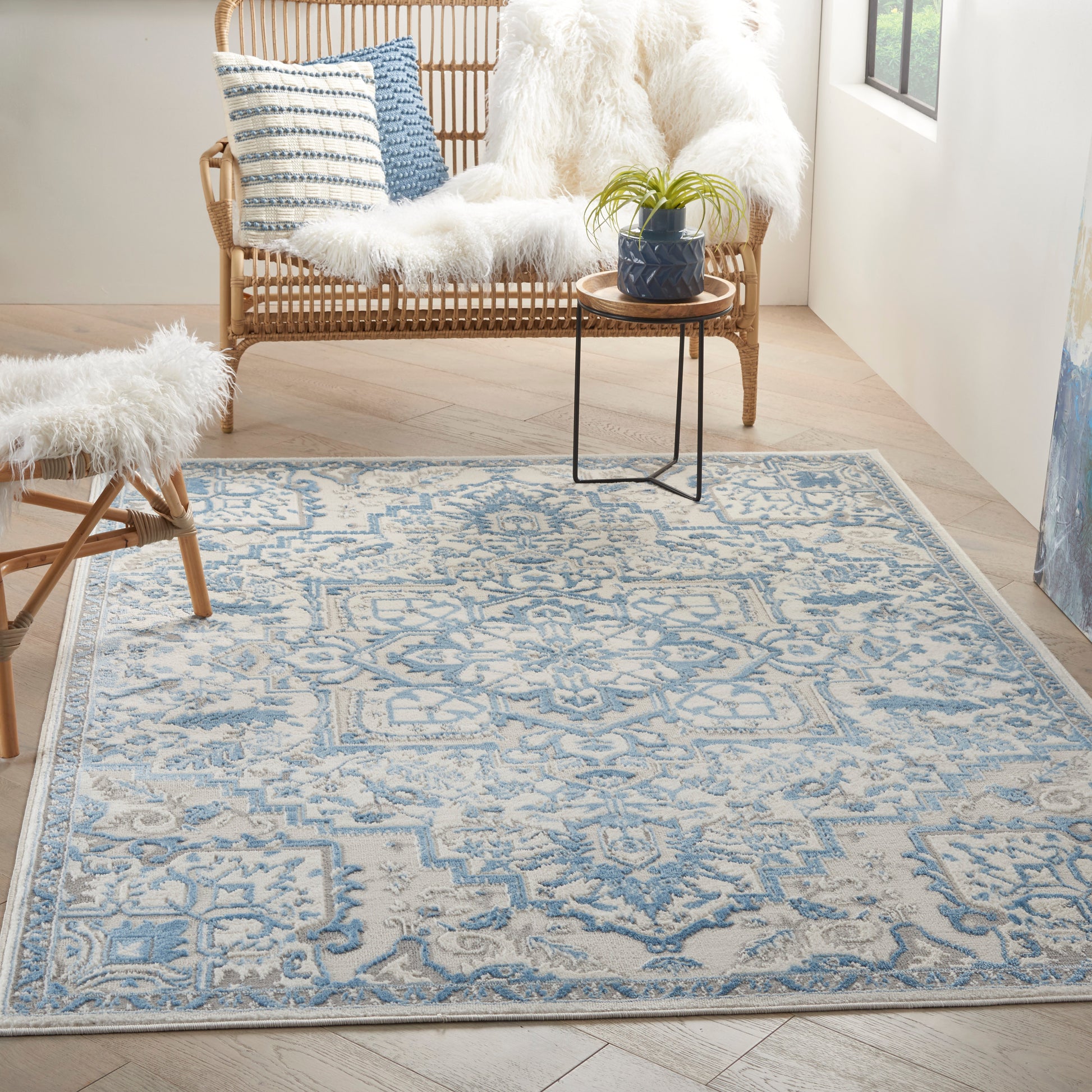 Rectangular blue and beige patterned area rug with geometric motifs, set in a sunlit room with wicker seating.