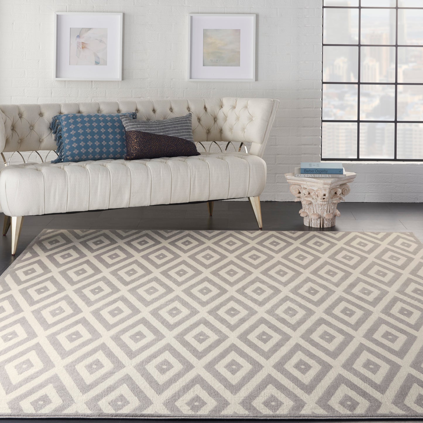 Beige geometric rug, 8' x 10', in a cream Mid-Century Modern style, on the floor with a white brick wall, framed art, and a pedestal side table in the background.
