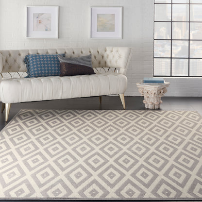 Beige geometric rug, 8' x 10', in a cream Mid-Century Modern style, on the floor with a white brick wall, framed art, and a pedestal side table in the background.