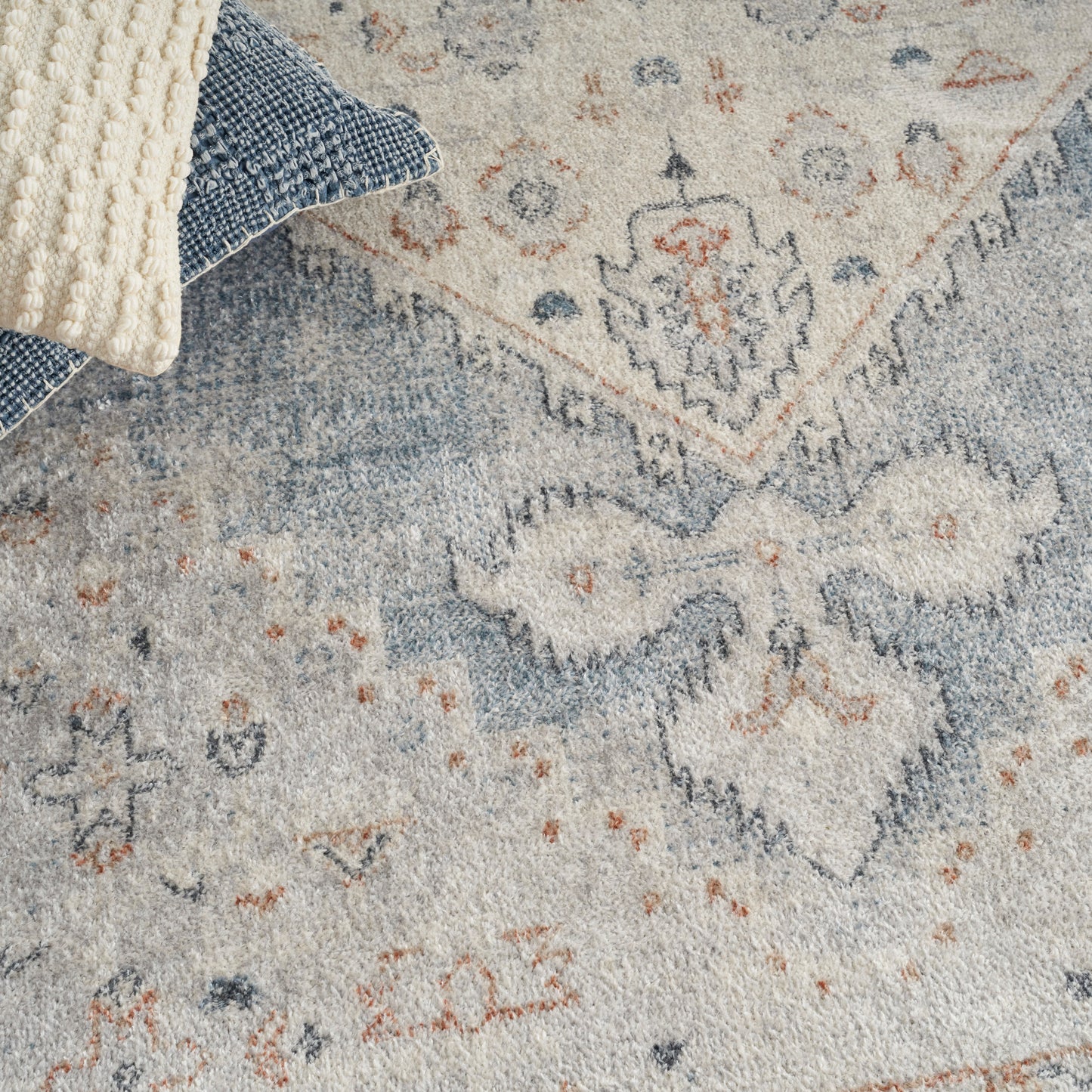 Distressed blue & cream oriental rug with orange accents, paired with cream chunky knit & blue woven pillows.