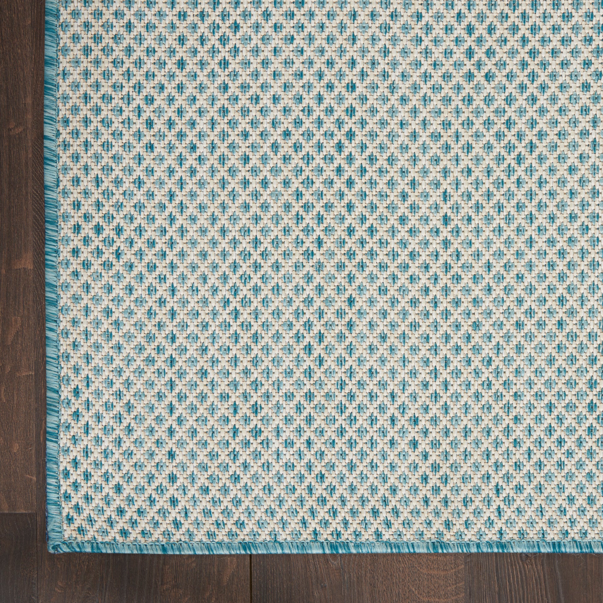 Blue and cream woven rug with diamond lattice pattern, teal border, fringe along edges on a dark wooden floor.