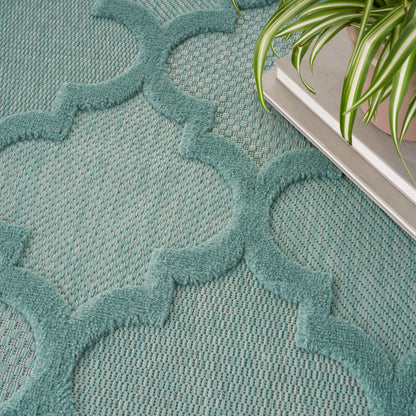 Teal rug with raised quatrefoil lattice pattern on woven base; contemporary decor with a potted plant nearby.