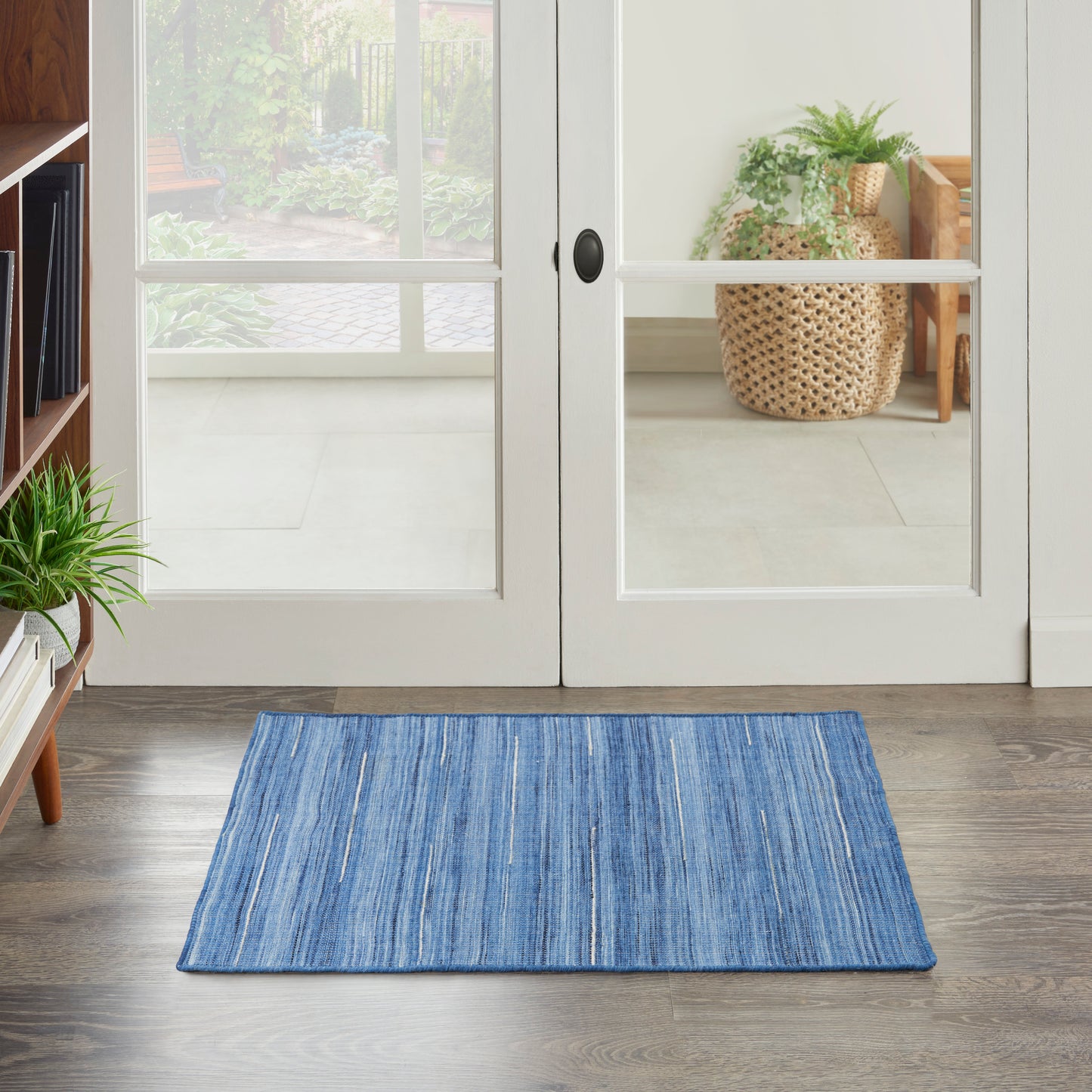 Blue striped rectangular entry rug on wood floor in front of glass French doors, with potted plants nearby.