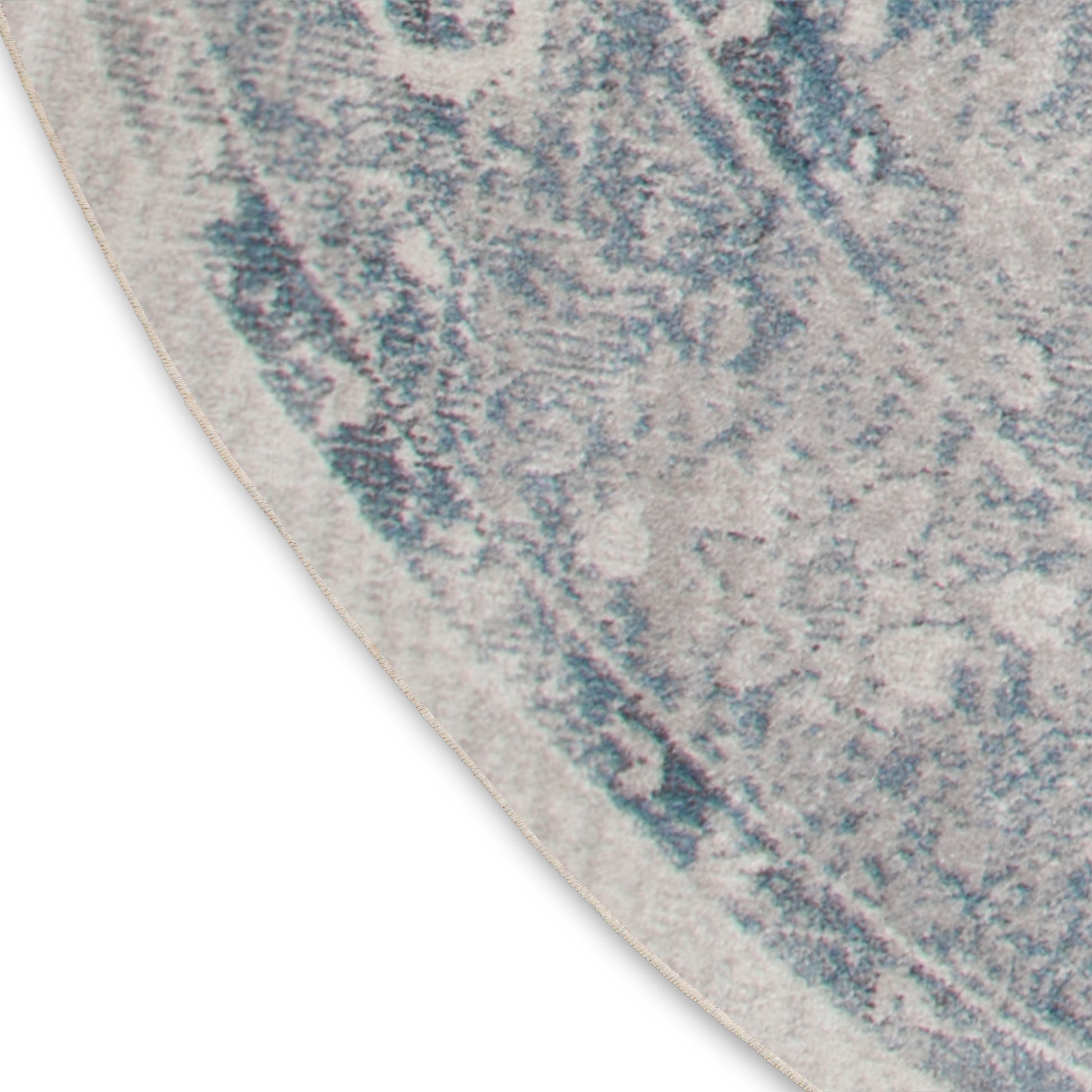 Curved edge close-up of a blue-gray abstract patterned round rug with cream background and plush texture.