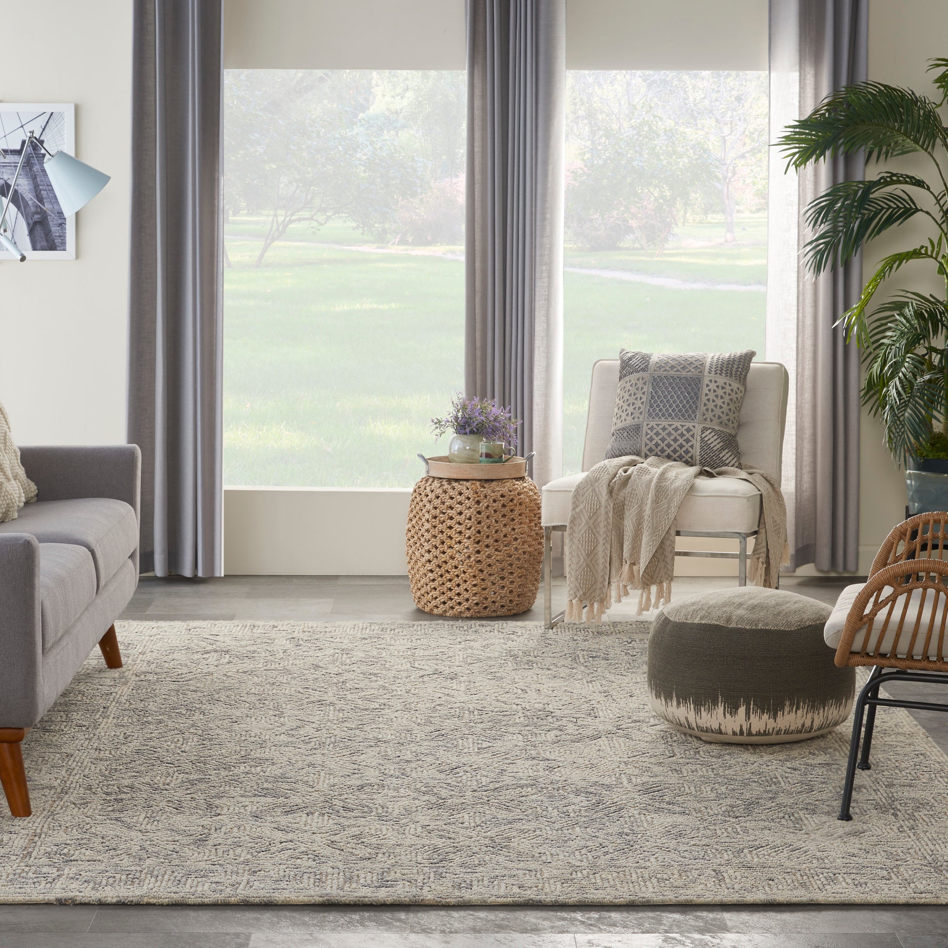 Neutral living room with gray sofa, cream armchair, woven rattan table, knitted throw, textured rug, round pouf.