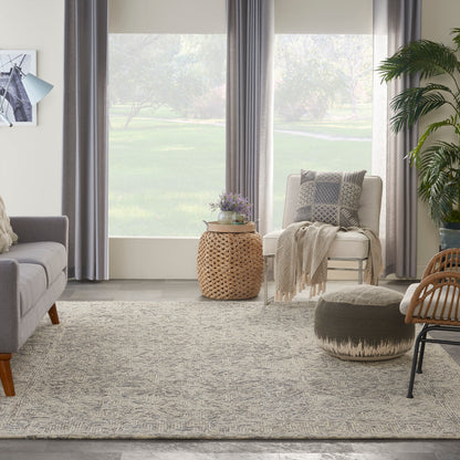 Neutral living room with gray sofa, cream armchair, woven rattan table, knitted throw, textured rug, round pouf.