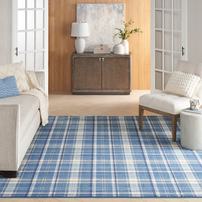 Rustic dark wood sideboard on warm wood wall, blue plaid rug, beige sofa and white armchair in airy living room.