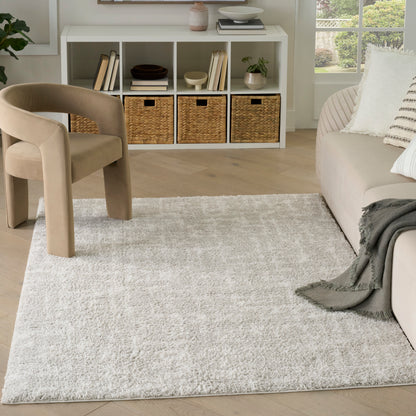Neutral living room with beige curved chair, white cubby storage with baskets, plush gray rug, beige sofa.