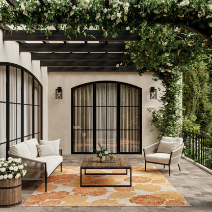 Patio with beige stucco walls, black arched doors, light cushions, wooden coffee table, orange tropical rug, greenery.