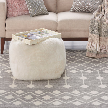 Fluffy white faux-fur pouf with a light wood tray on top, beige sofa and gray patterned rug in a cozy living room.
