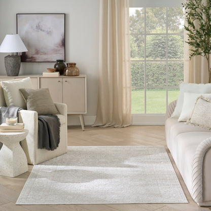 Ivory textured area rug with subtle border in a neutral beige living room with cream sofa and light wood floor.