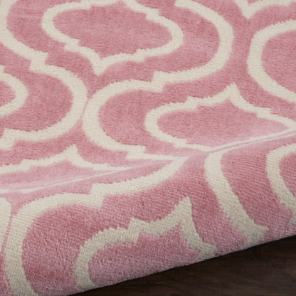 Soft pink plush rug with white geometric trellis pattern, curling lattice shapes on dark wood floor.