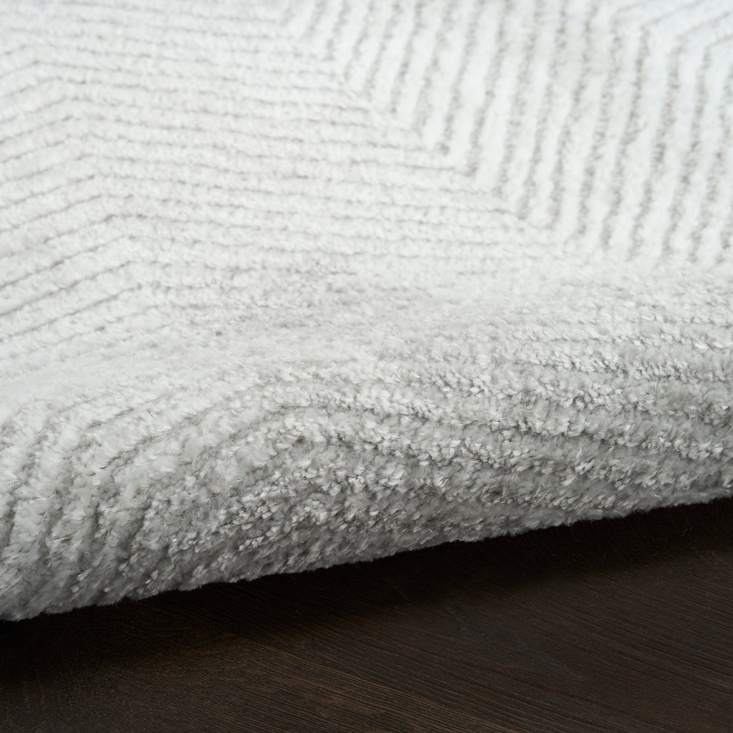 Close-up of a soft white rug with diagonal ribbed pattern on a dark wood surface.