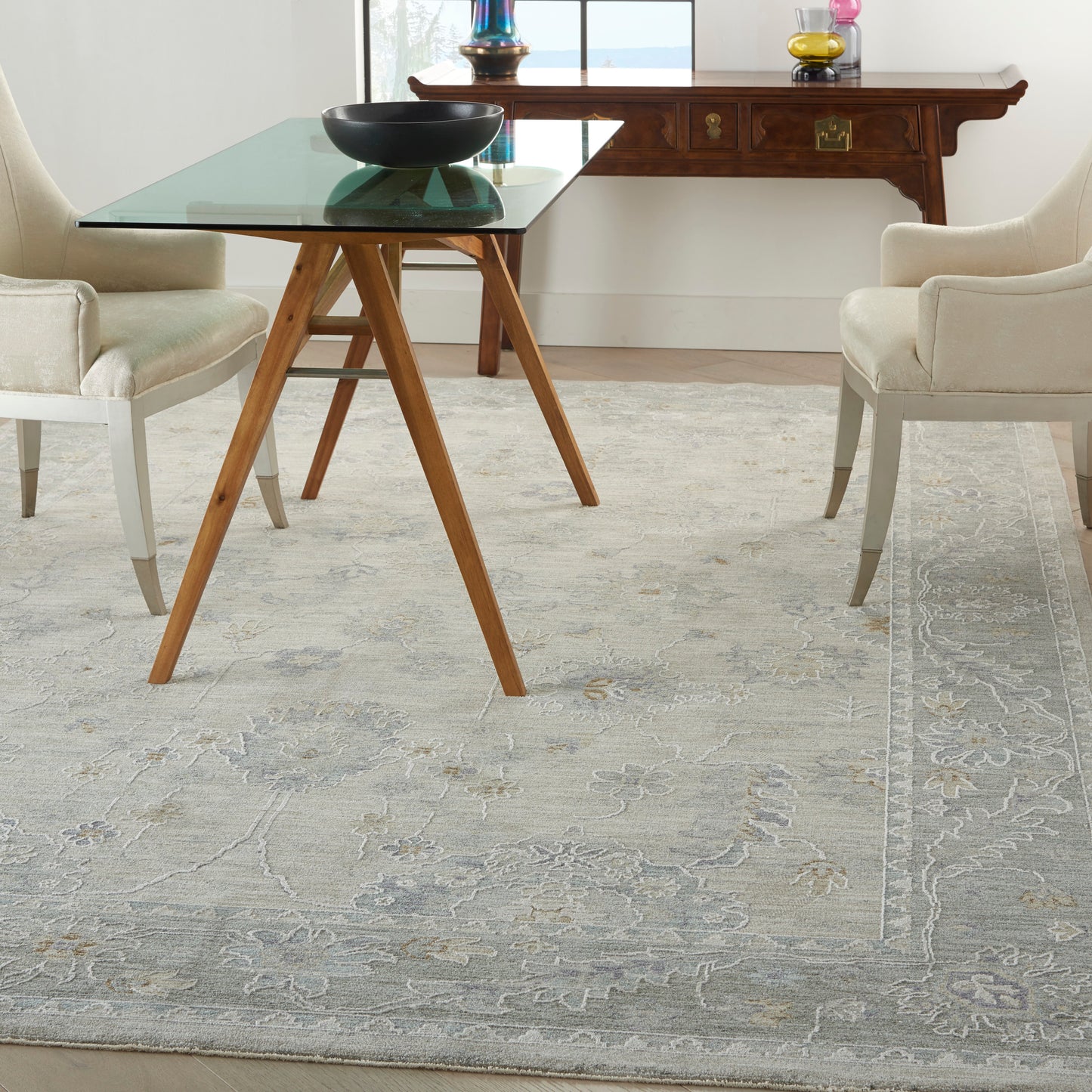 Glass-top dining table with angled wooden A-frame legs in mid-century style, flanked by beige upholstered chairs.