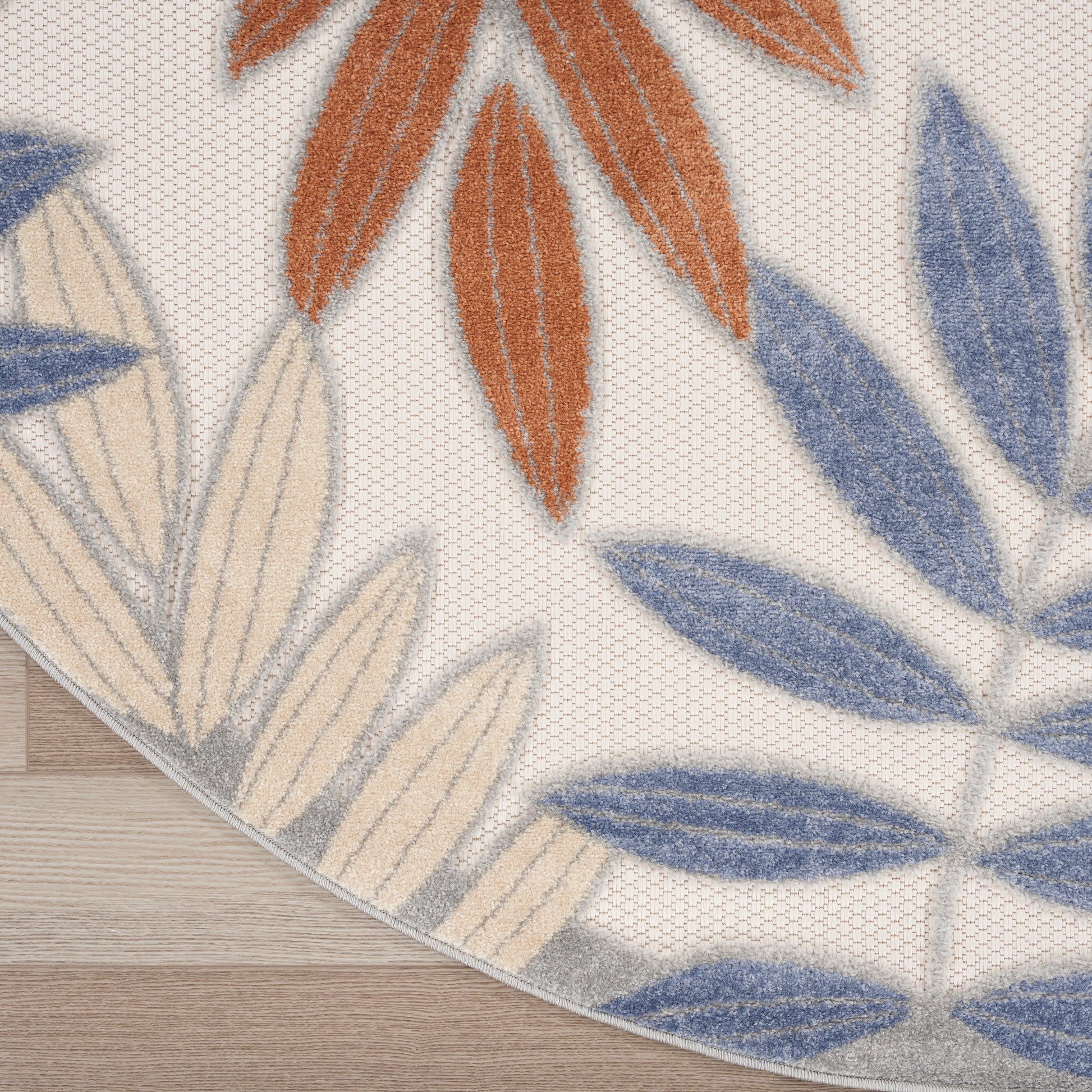 Round area rug with blue, orange and cream leaf motifs on beige textured background; plush, soft pile.