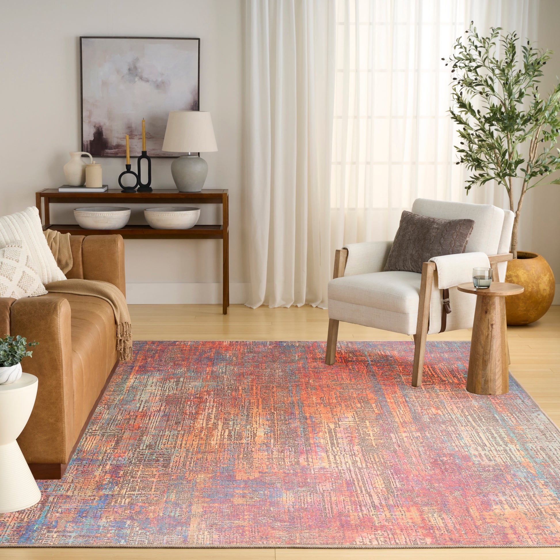 Cozy living room with a vibrant abstract rug, tan leather sofa, white armchair, wooden side table, and potted plant.