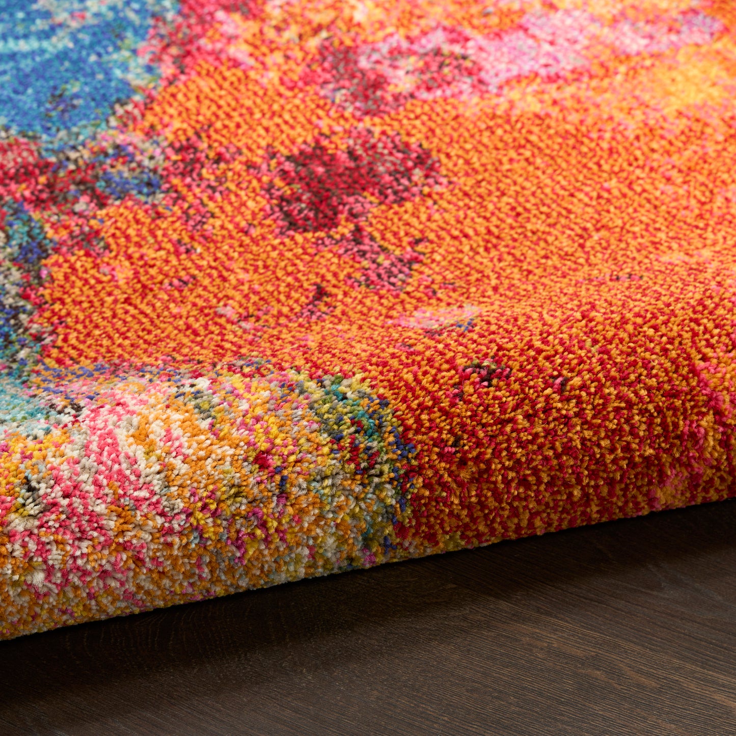 Close-up of a vibrant tufted rug with orange, pink, blue and yellow hues, thick pile edge on dark wood floor.