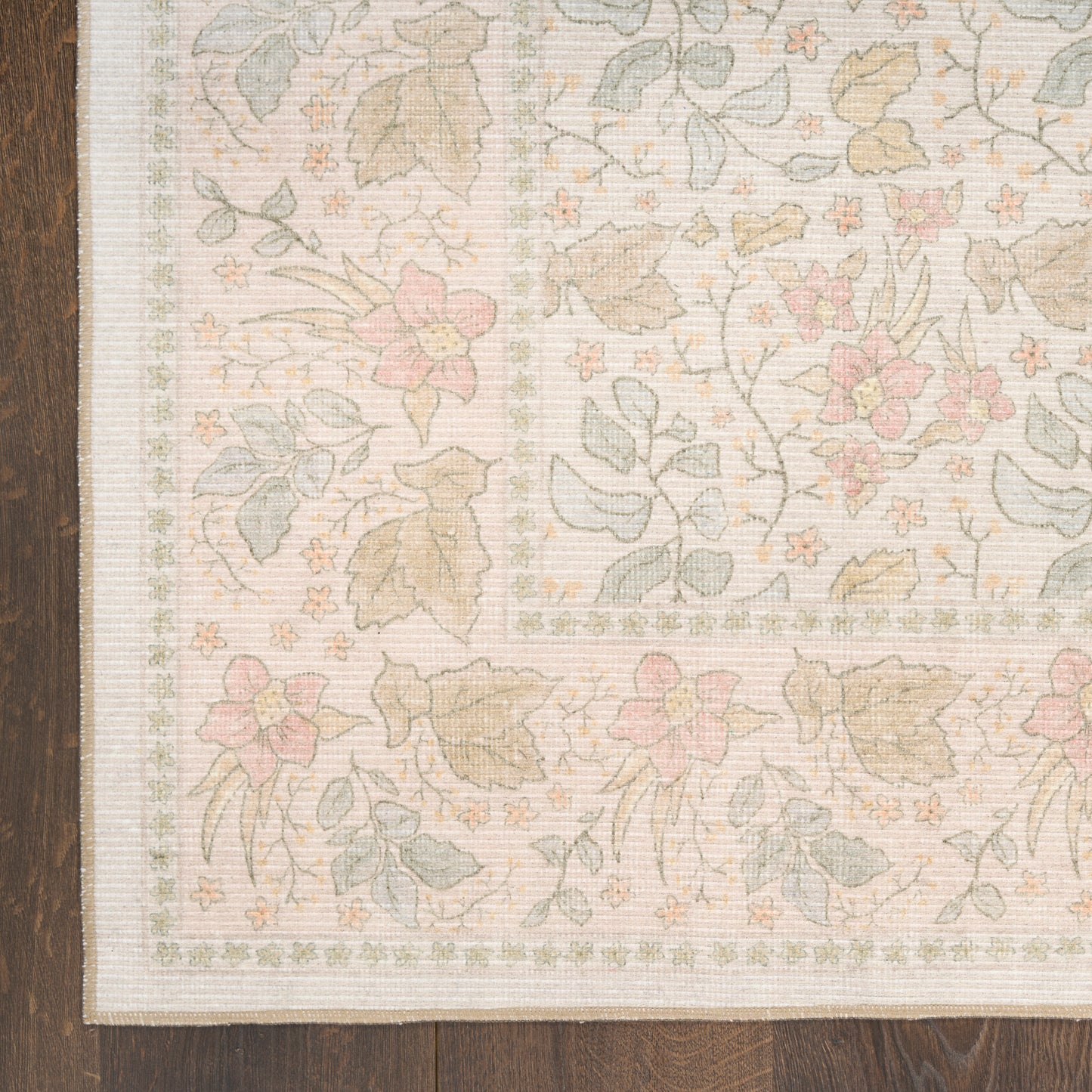Pastel floral area rug with pink flowers and green leaves, beige border, on dark wooden floor.