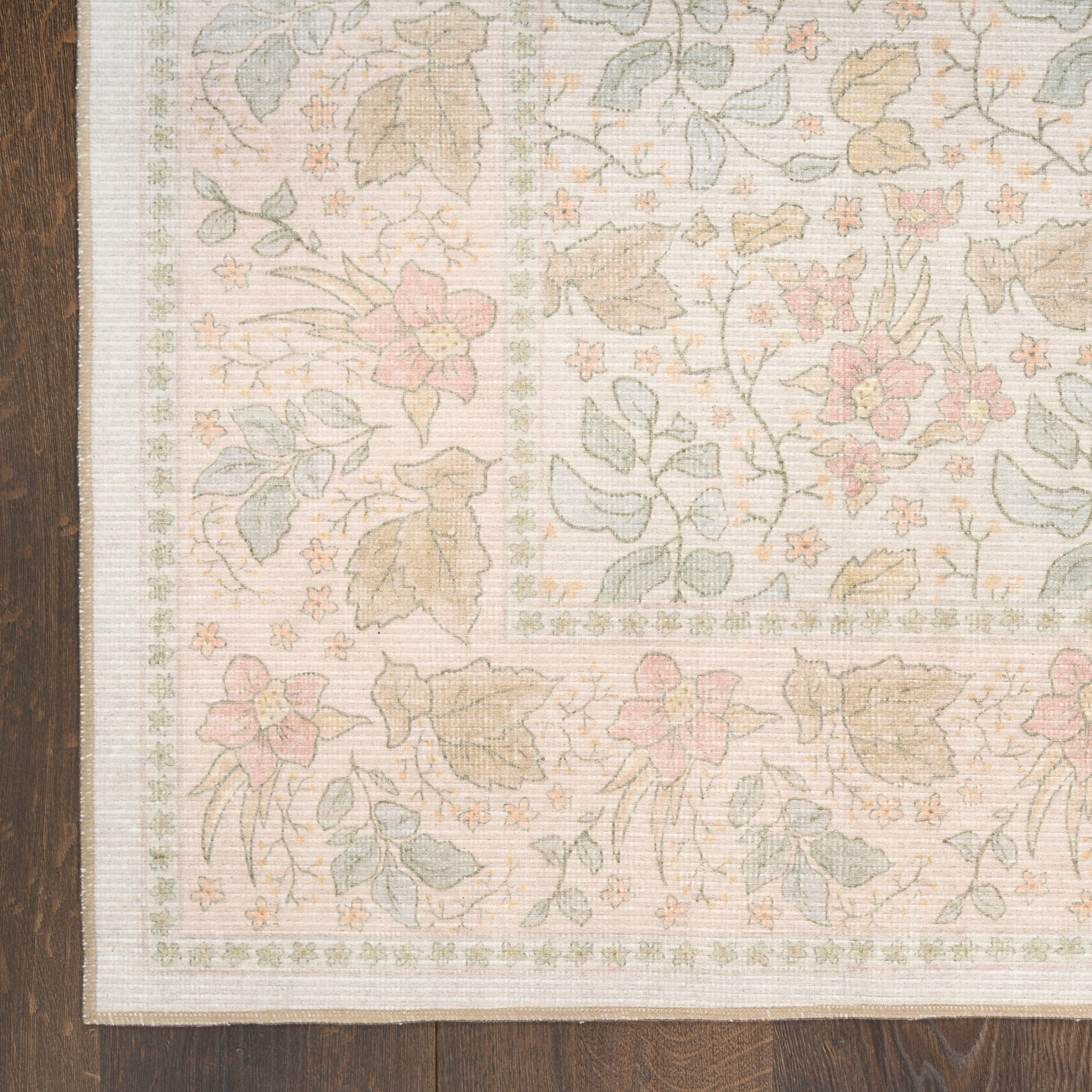 Pastel floral area rug with pink flowers and green leaves, beige border, on dark wooden floor.