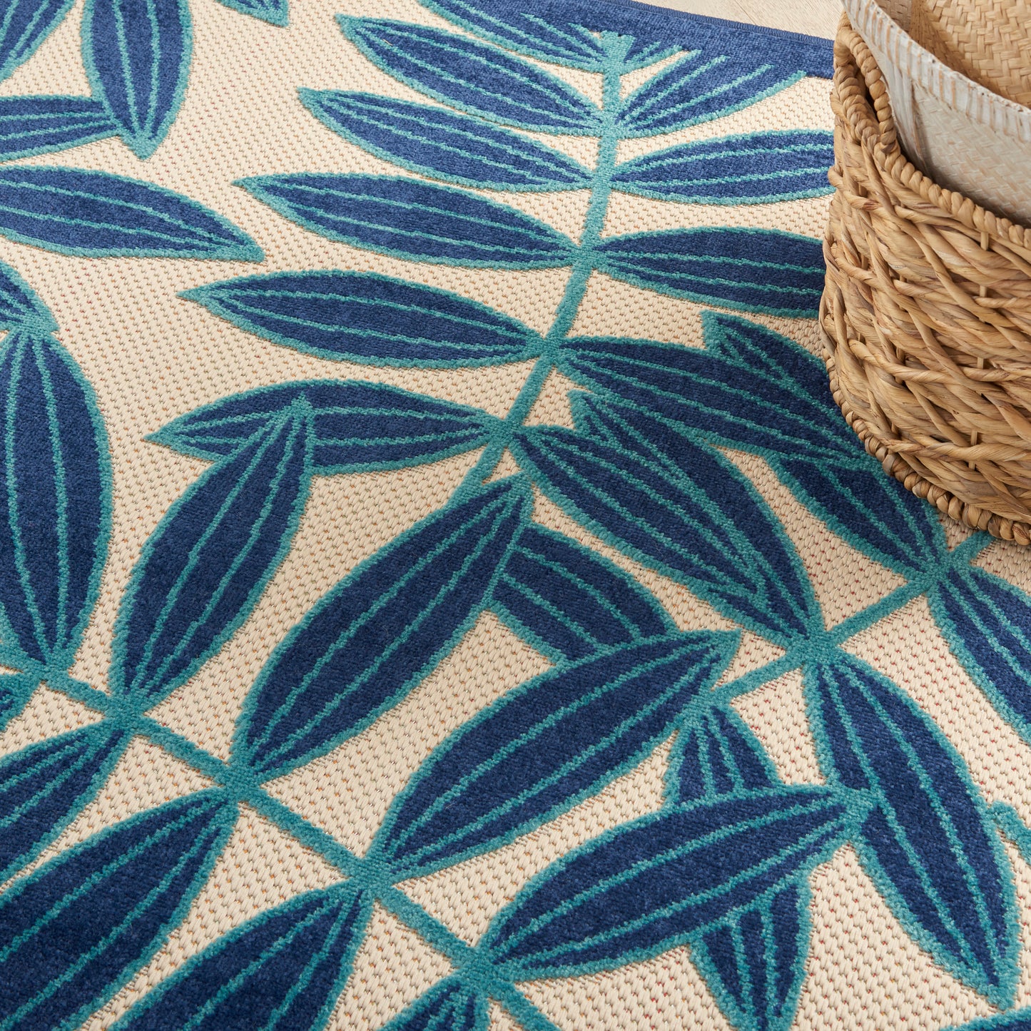 Blue palm-leaf patterned rug on a beige woven background with a partial wicker basket.