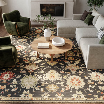 Living room with dark floral rug, round wooden coffee table, gray sectional sofa, green armchairs, fireplace & plant.