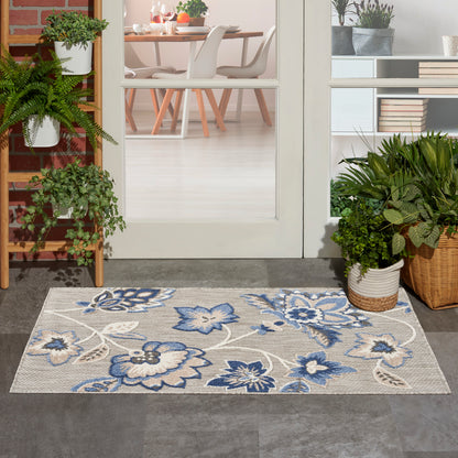 Gray rectangular floral rug with blue flowers at the doorway, flanked by potted plants and a dining room visible inside.