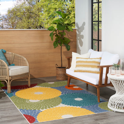 Outdoor rug with yellow, green, blue and orange circles; paired with wicker chair and white cushioned sofa.
