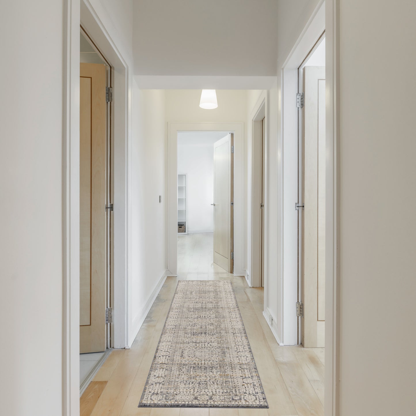 Bright hallway with light wood floor, white walls, natural wood doors, and a beige patterned runner rug under a soft pendant light