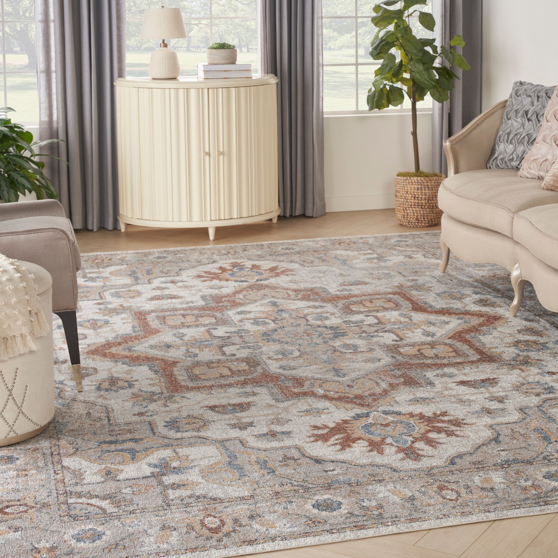 Beige, blue, and rust patterned area rug in a bright living room with cream sofa, curved cream cabinet, and a potted plant.
