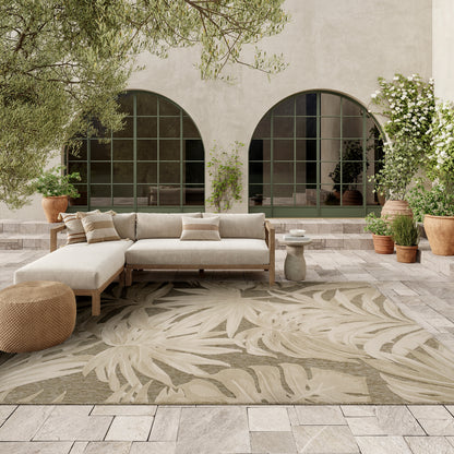 Beige outdoor sectional sofa with a wooden frame on a leaf-pattern rug, arched green-framed windows and potted plants.