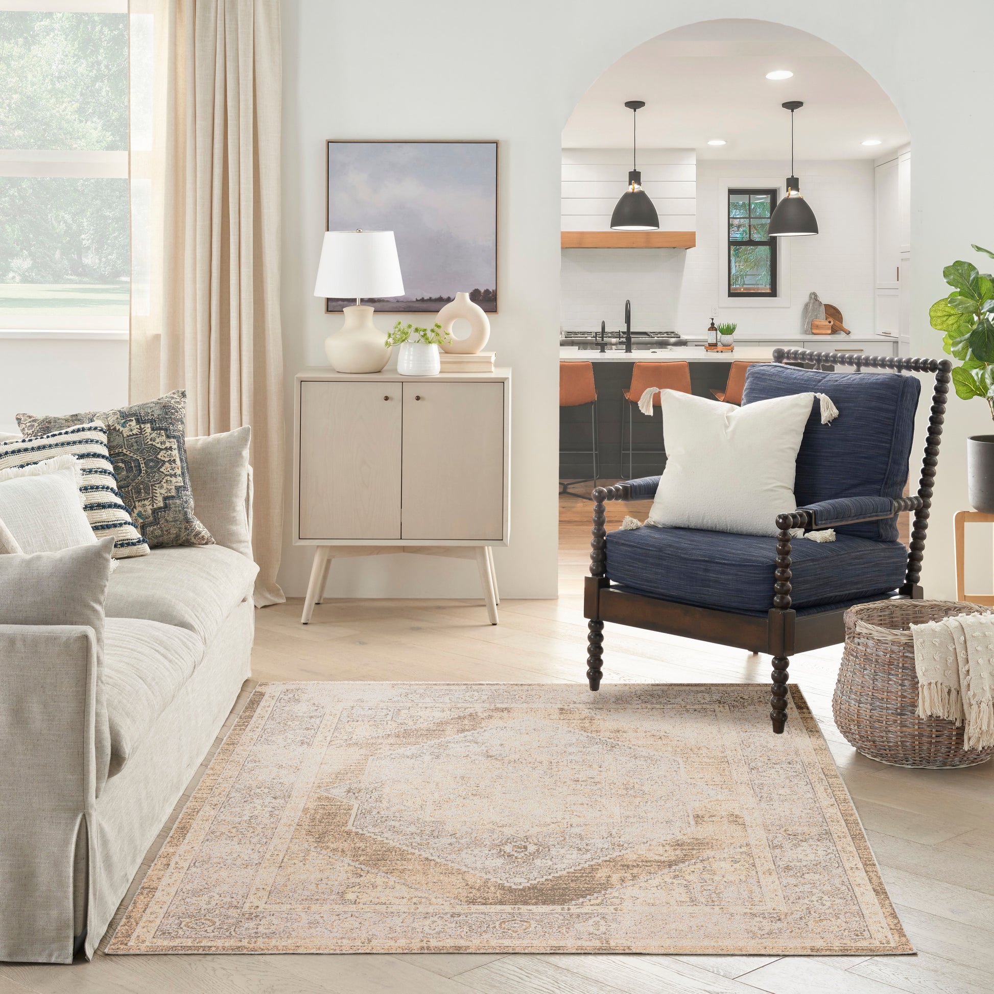 Neutral living room with cream sofa, navy spindle-armchair, beige patterned rug, light wood cabinet, arched kitchen doorway.