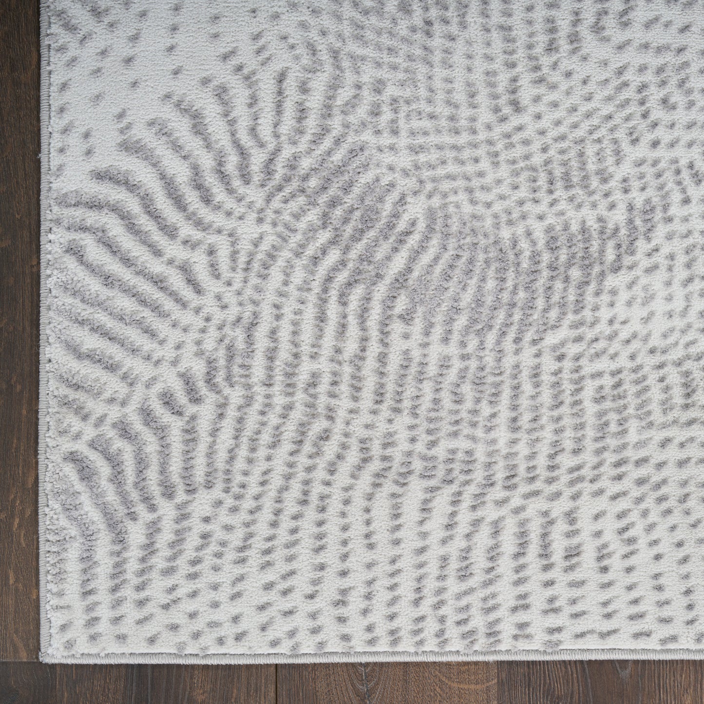 Light gray and white abstract patterned rug with soft pile on dark wood floor; modern living room style.