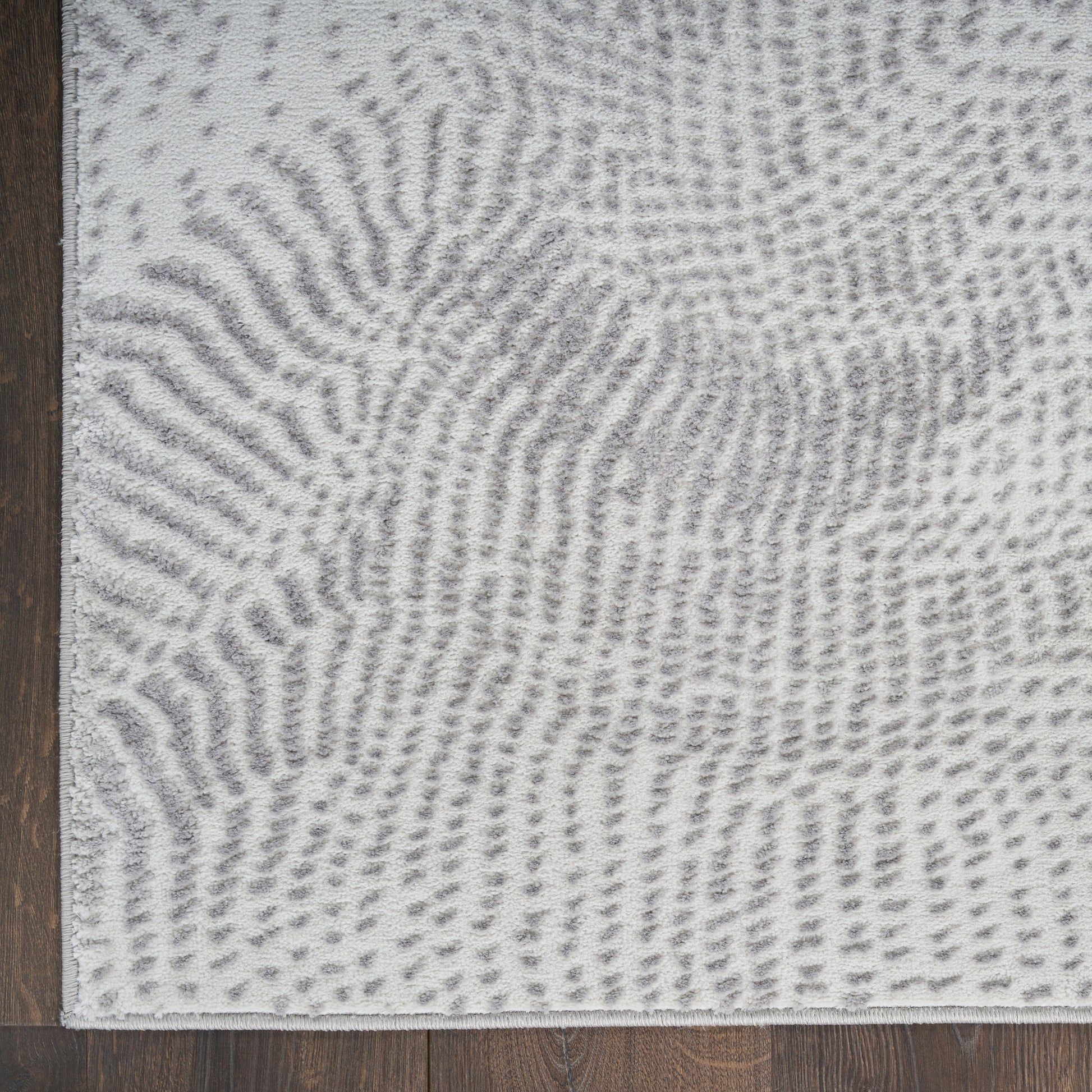 Light gray and white abstract patterned rug with soft pile on dark wood floor; modern living room style.