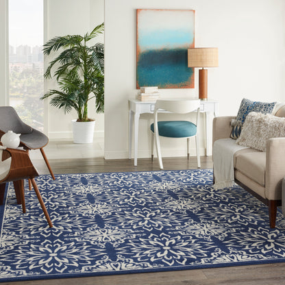 Blue floral area rug anchors a bright living room with white desk, teal chair, beige sofa, plant, and abstract blue art