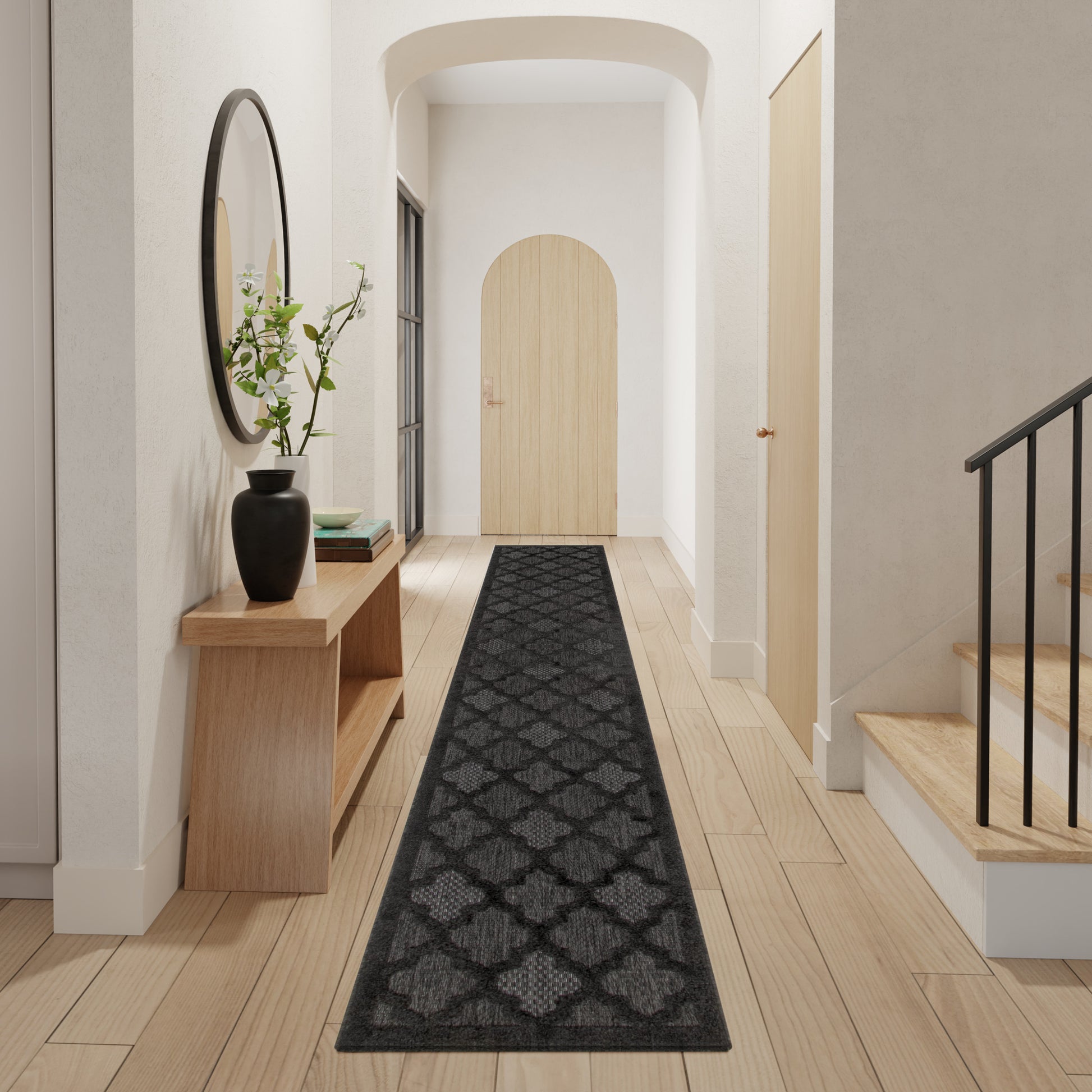 Modern hallway with light wood floors, black geometric rug, wooden console with vase, arch doorway, stairs.