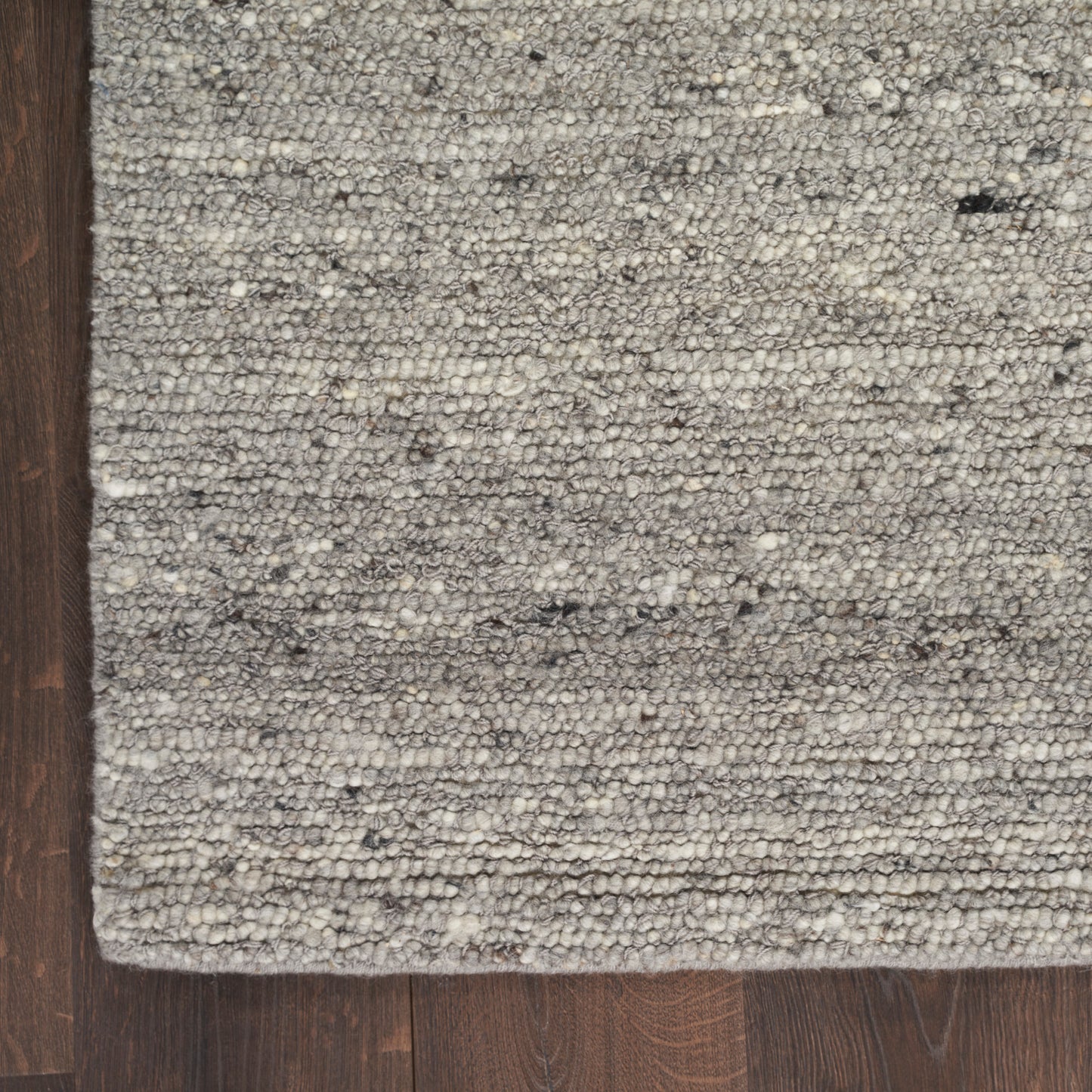 Rectangular grey speckled loop-pile area rug on dark wood floor with neutral textured weave.