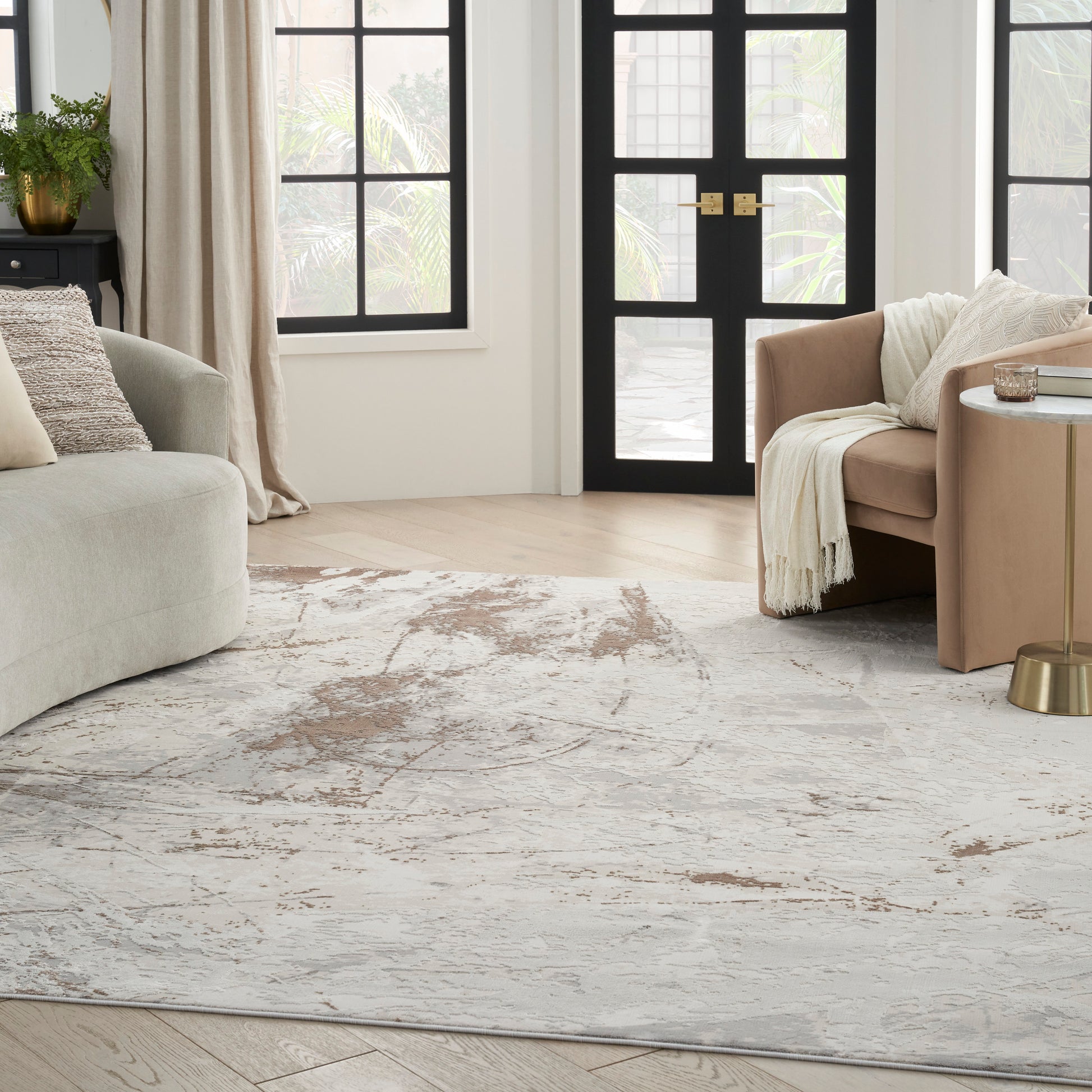 Neutral living room with beige fabric sofas, cream throw, gold side table, abstract gray rug, black framed doors and big windows.