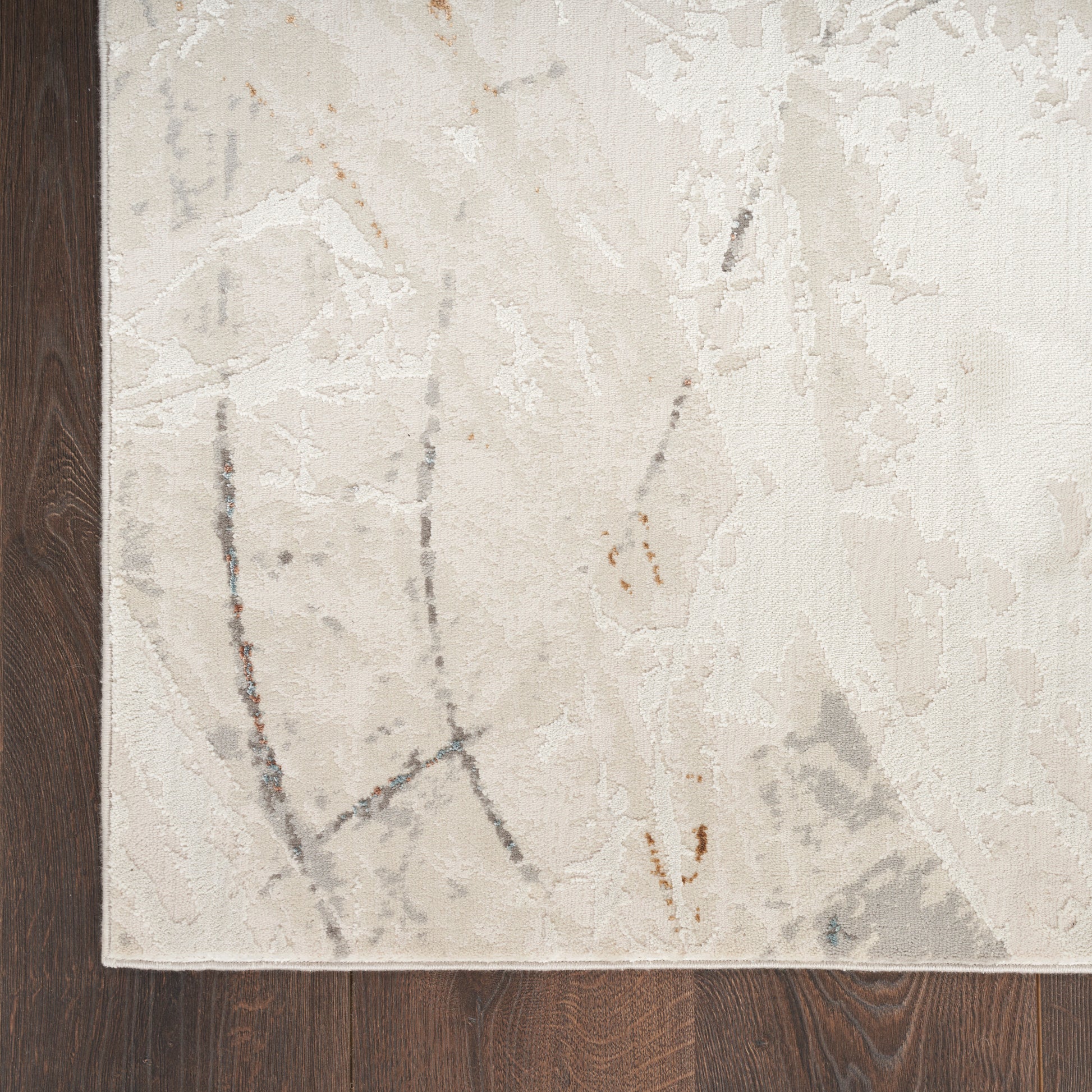 Cream area rug with subtle gray and rust-brown abstract marble pattern on dark wood floor.