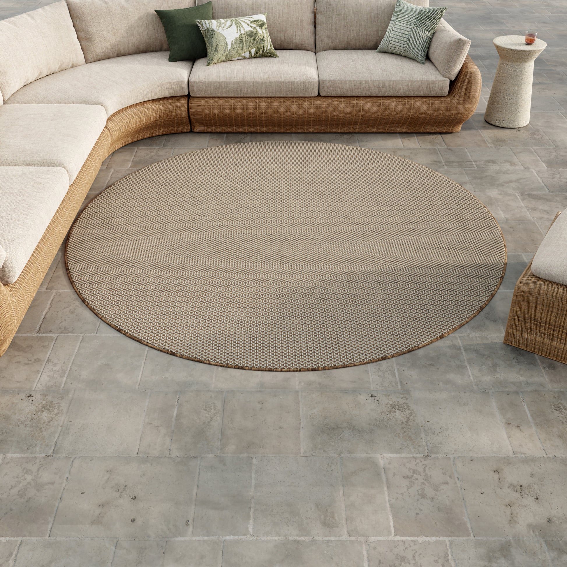 Round beige woven outdoor rug on gray tiled patio with a curved beige sectional wicker sofa and neutral cushions.