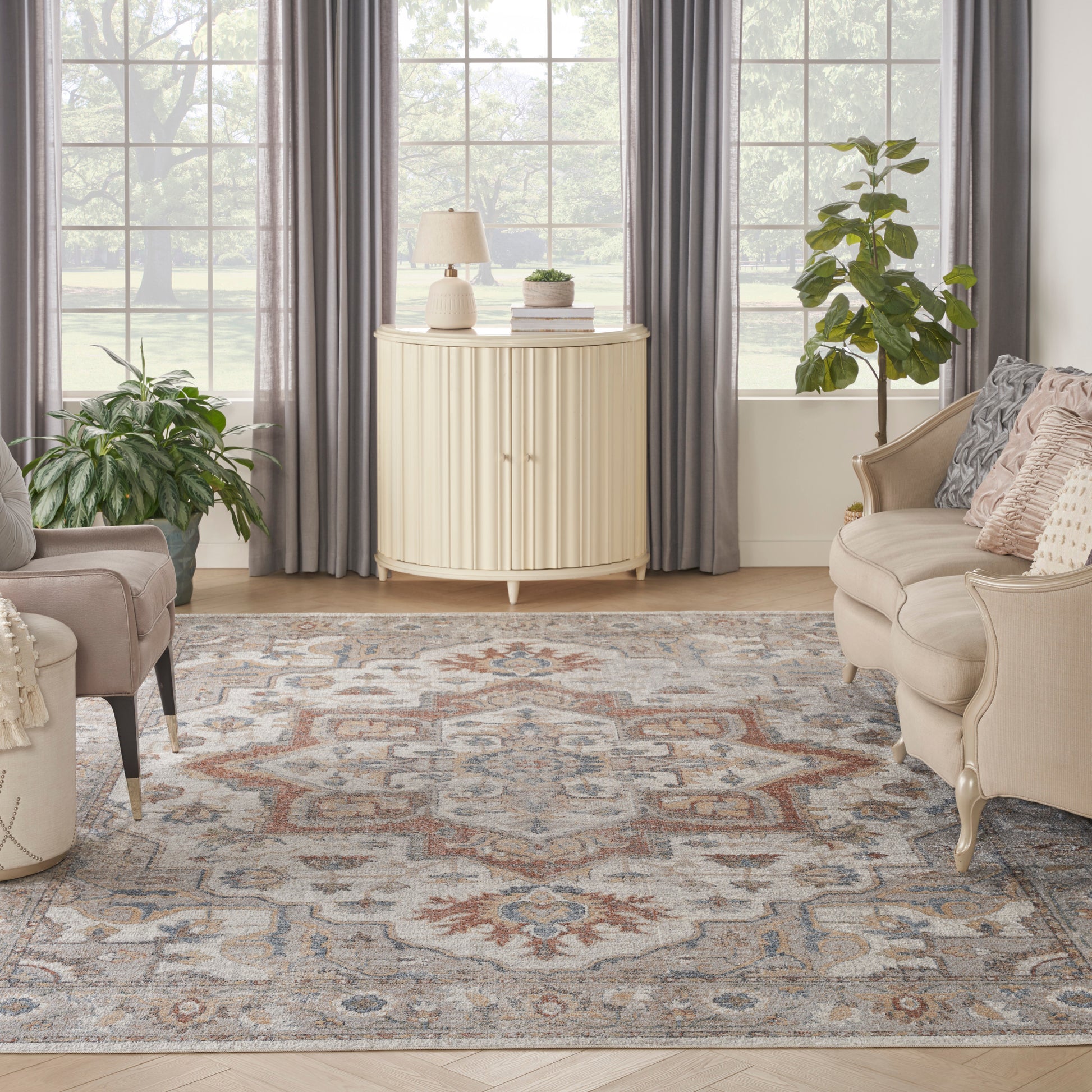 Cream-toned vintage rug on a living room floor with beige sofas, green plants, muted blue-gray accents, and gray curtains.