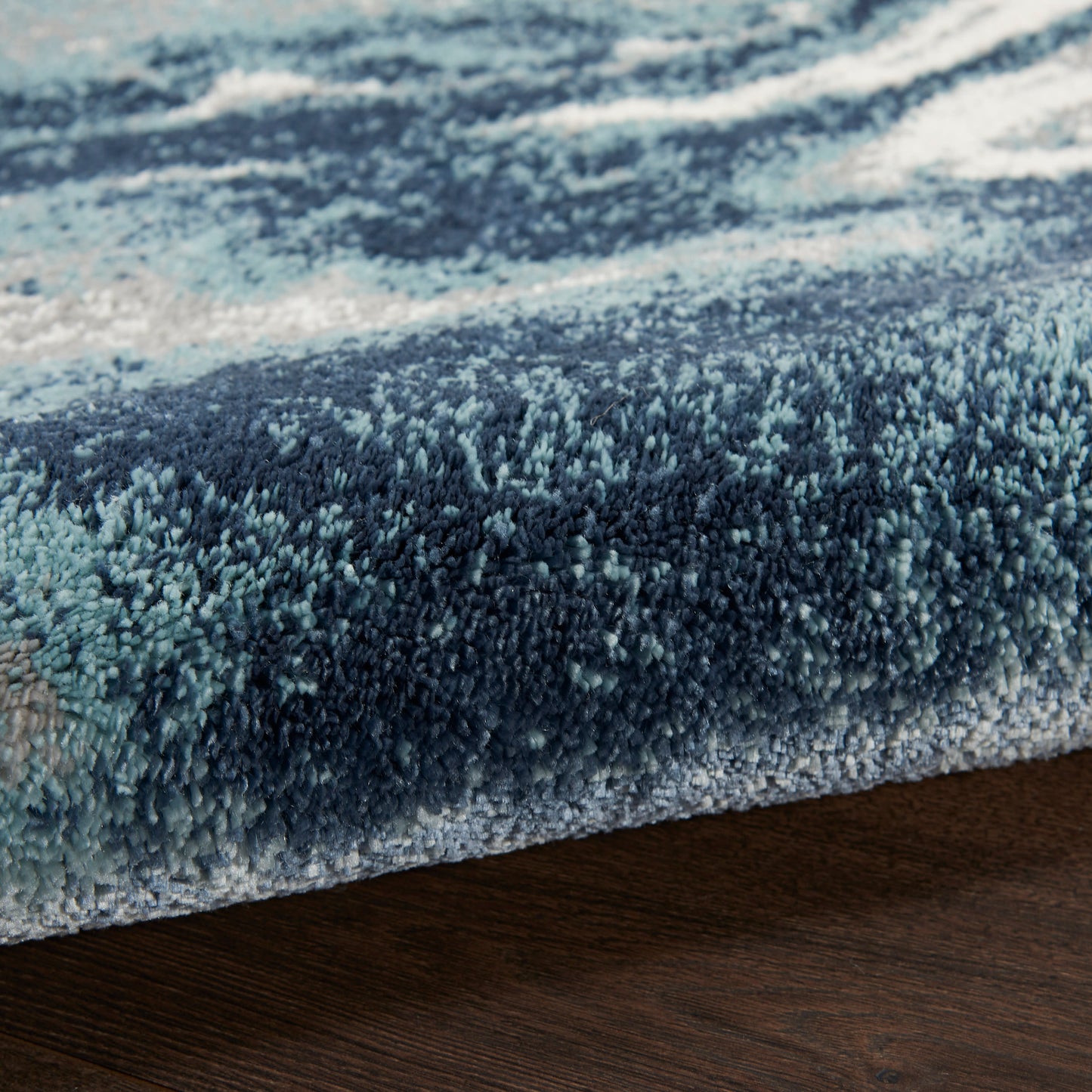 Close-up of a blue shag rug with gradient navy to light blue, edge resting on dark wood floor.