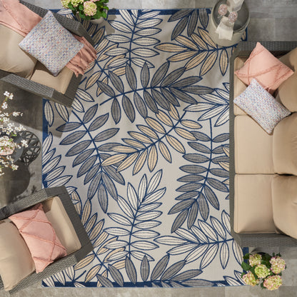 Rectangular rug with blue and navy botanical leaf pattern on a light beige background, in a cozy living room with sofas.