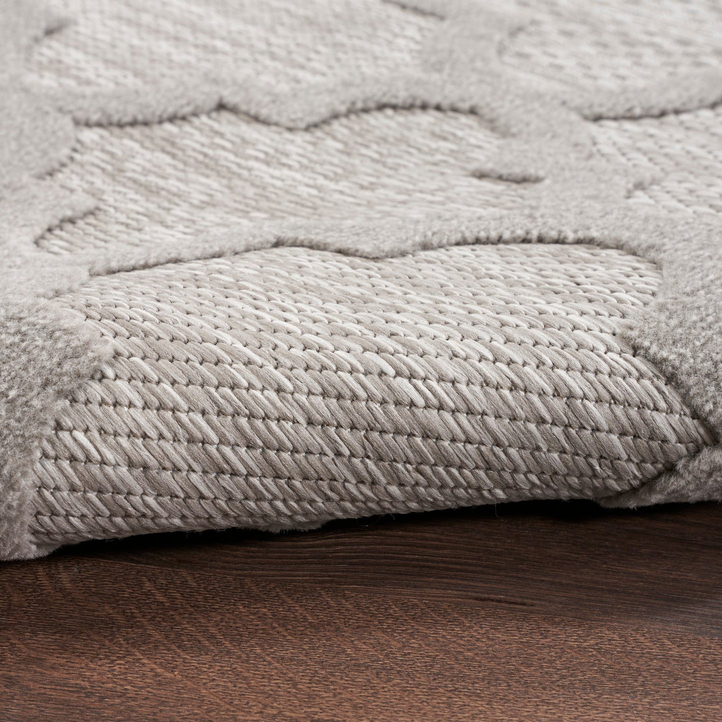Light gray plush rug with a wavy cloud pattern and raised texture, folded edge on dark wood floor.