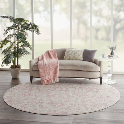 Round pink-patterned rug in a bright modern living room; beige sofa with a pink throw blanket and patterned cushions.