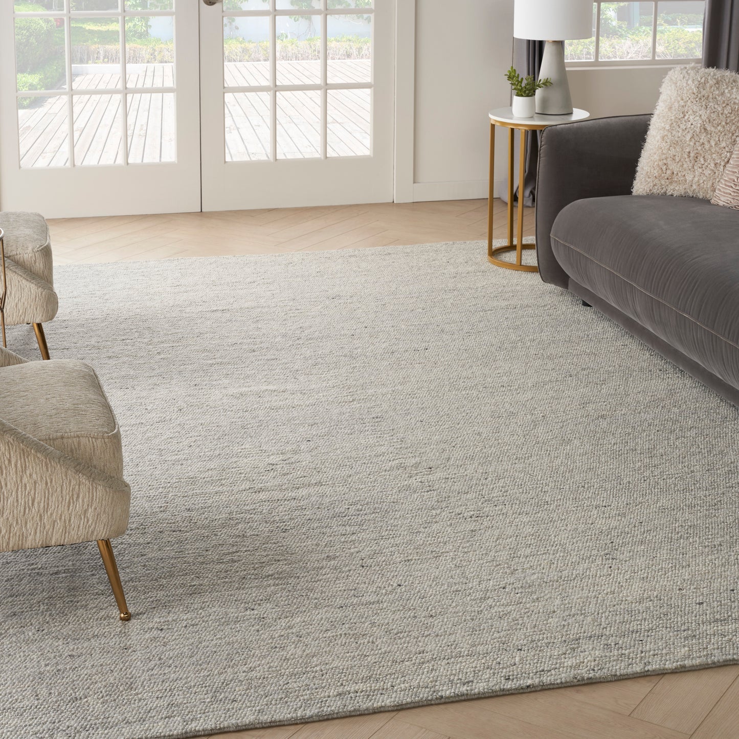 Light gray textured area rug on wood floor with beige upholstered chairs, a dark gray sofa, and a gold side table.