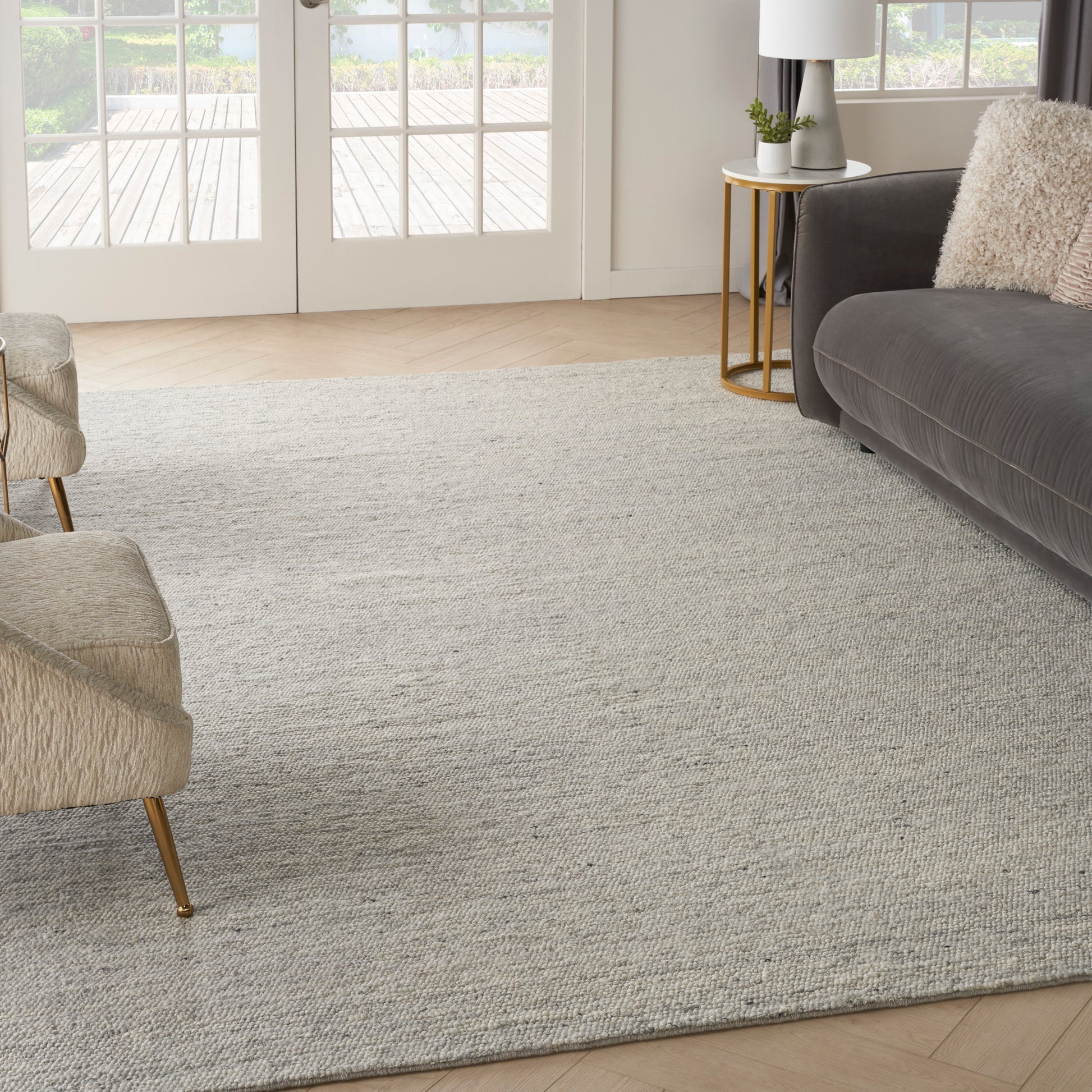 Light gray textured area rug on wood floor with beige upholstered chairs, a dark gray sofa, and a gold side table.